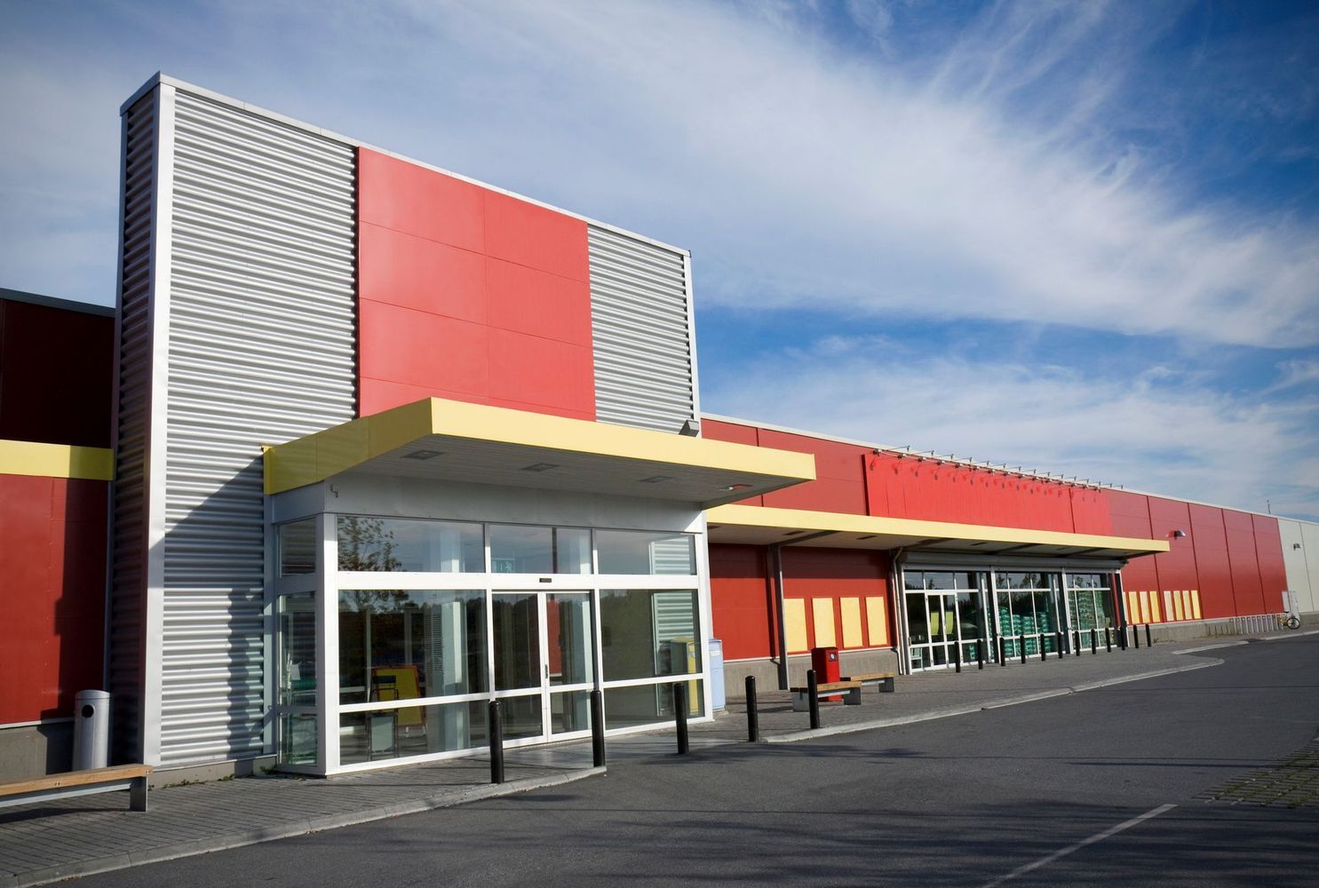 Modern building with red walls and a metal entrance canopy under a blue sky.