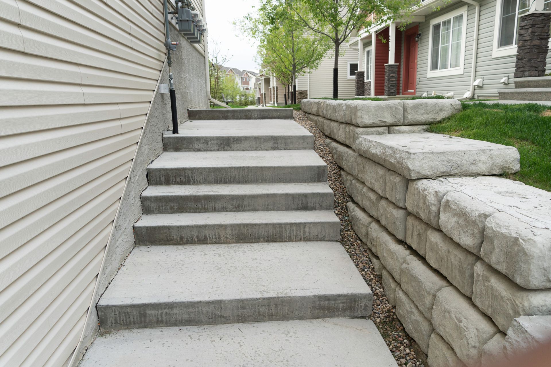 Concrete outdoor stairs beside a house and stone retaining wall in a narrow side yard