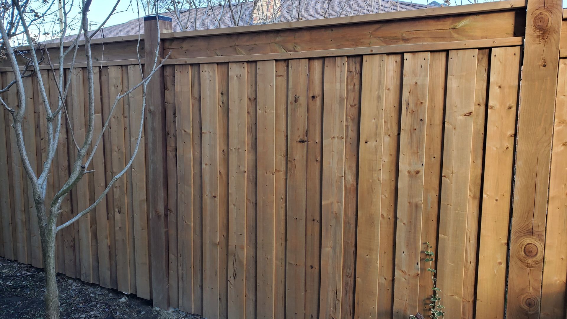 a wooden fence with a tree in the background and a roof in the background .