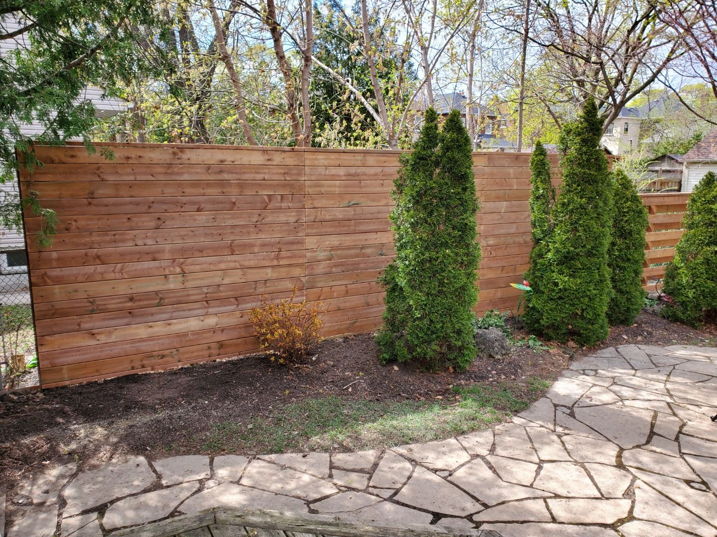a wooden fence surrounds a stone patio in a backyard .