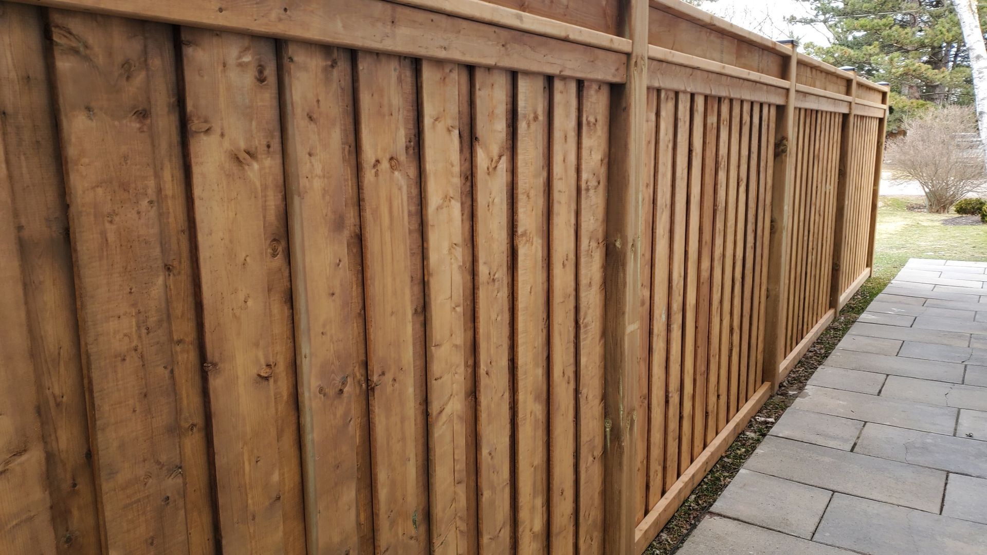 a wooden fence is sitting next to a brick walkway .