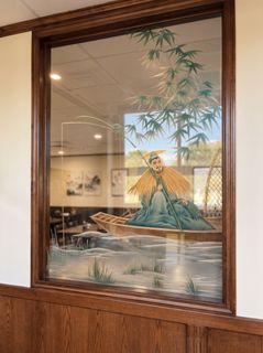 Framed mural of a seated figure on a dragon-like creature behind glass in a wood-paneled hallway