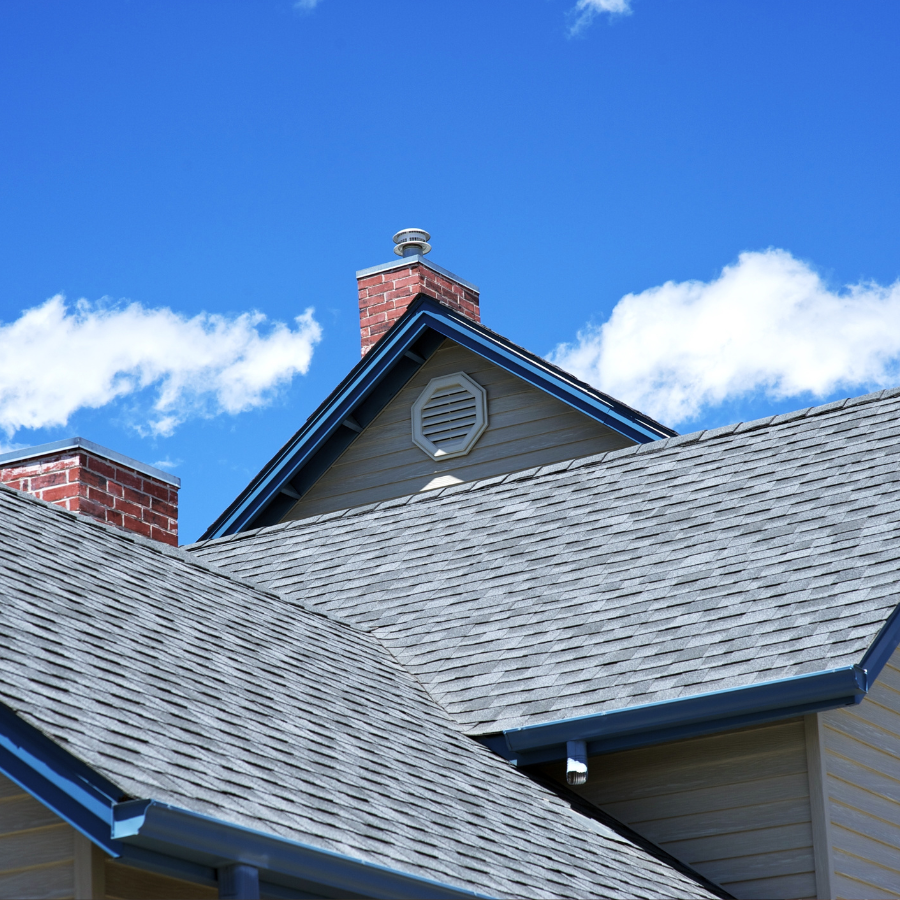 Rooflines of a house with gray shingles and blue trim against a bright blue sky