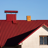 Red tiled roof with a small chimney against a blue sky, above a white house wall and window