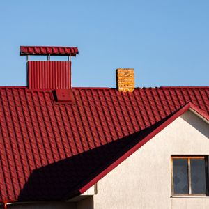 Red tiled roof with a small chimney against a blue sky, above a white house wall and window