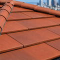 Worker in yellow hard hat repairing red roof tiles beside a window