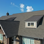 Aerial view of a house roof with gray shingles, dormer windows, and a blue sky