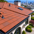 Worker installing roof shingles on a tiled roof, wearing a gray shirt and neon safety vest