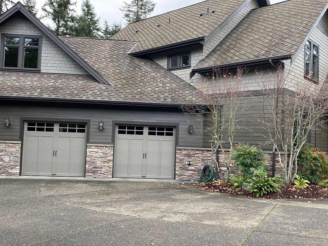 Gray painted garage and stone accents on craftsman-style home in wooded setting.