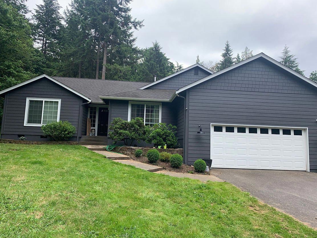 Single-story home with dark painted siding, white trim, and garden landscaping.