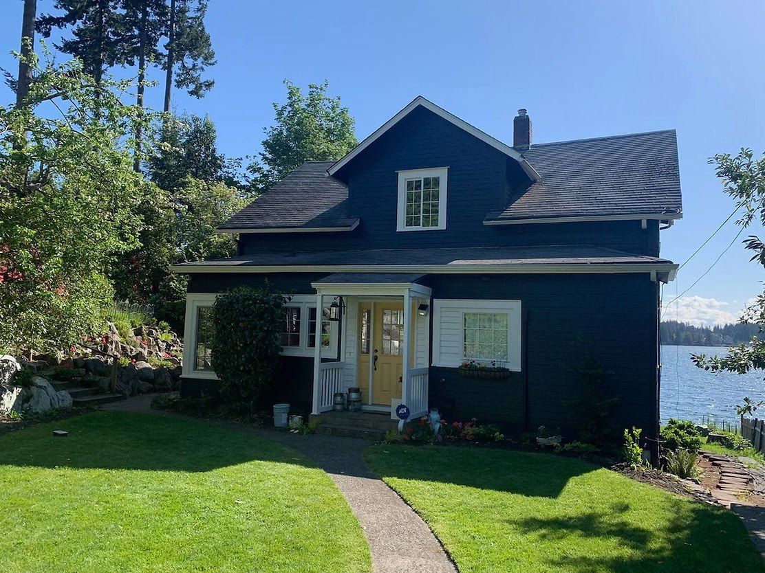 Dark blue waterfront home with freshly painted siding, white trim, and covered porch.