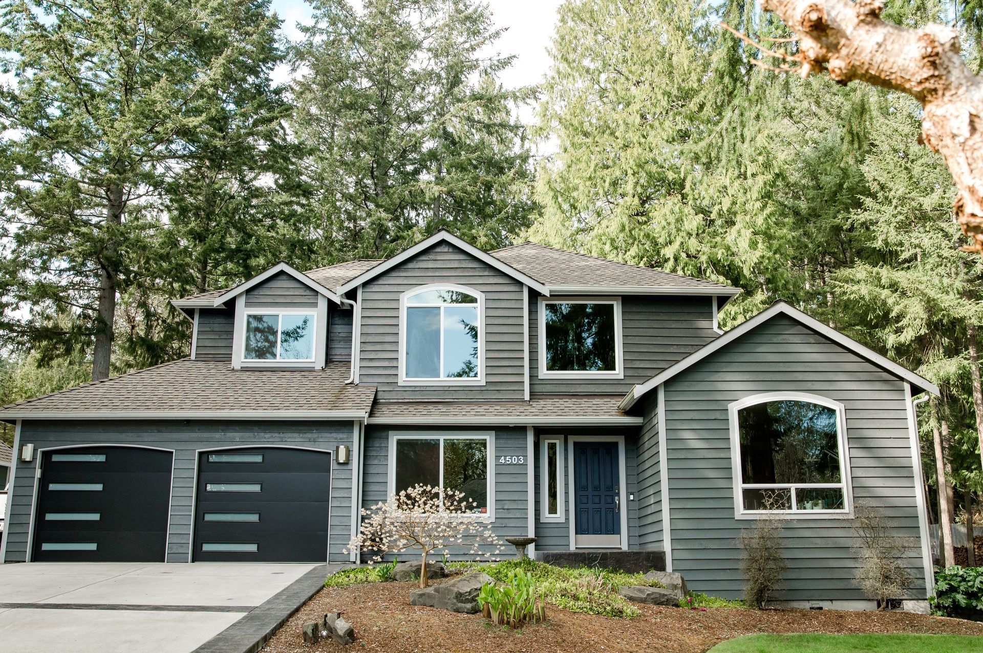 A large gray house with a blue door is surrounded by trees.