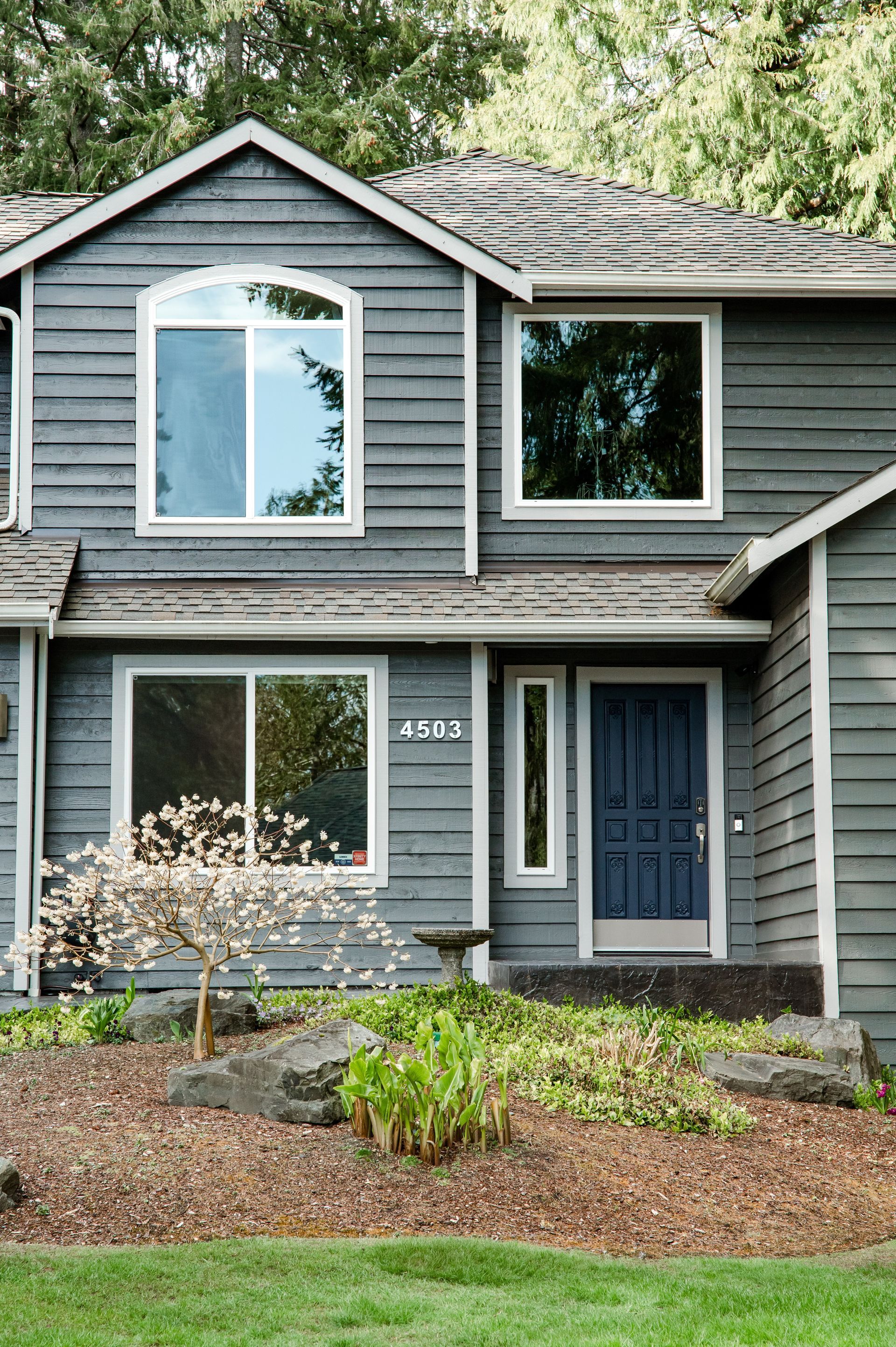 The front of a gray house with a blue door and windows.