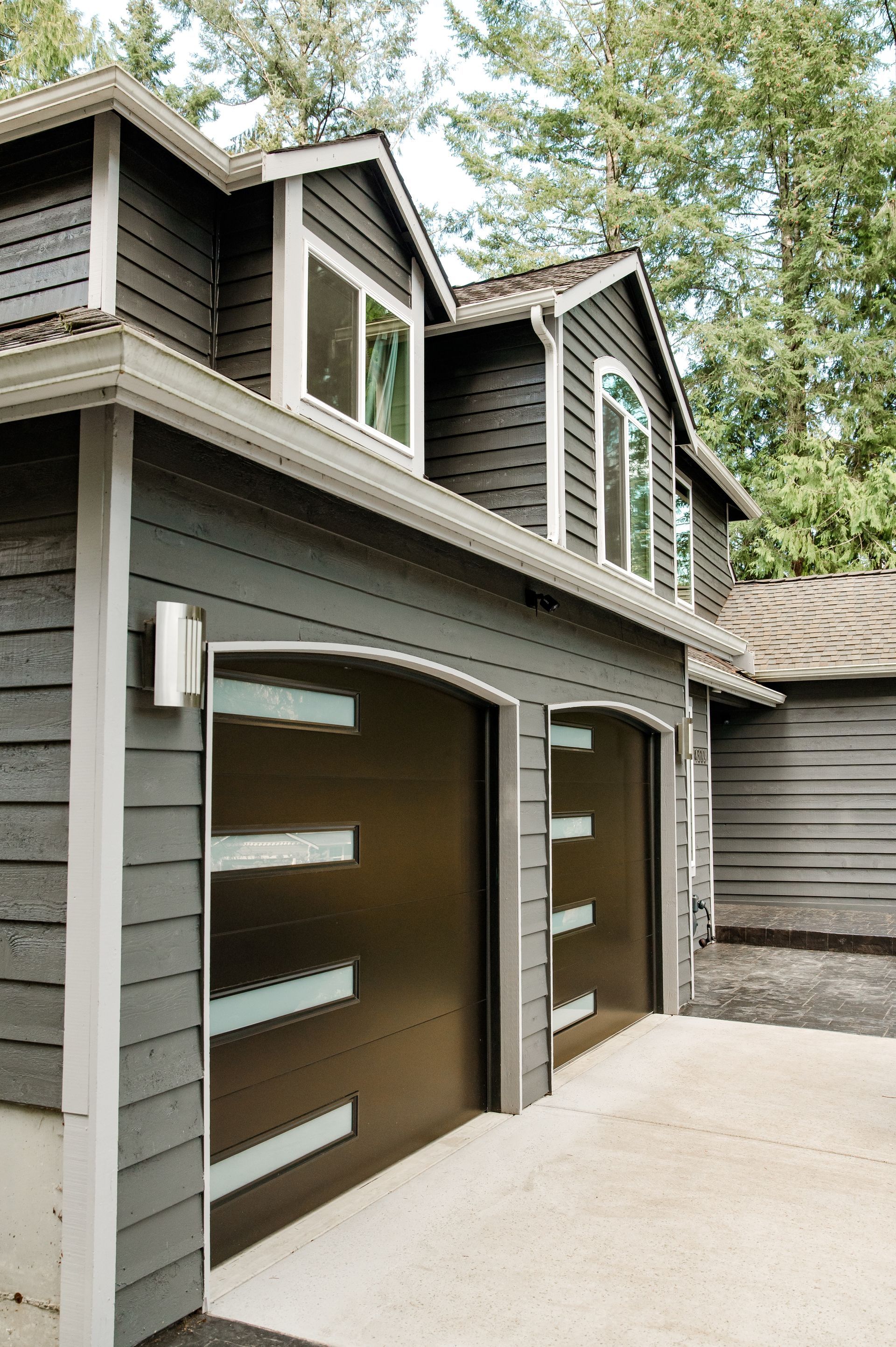A house with two garage doors and a roof with trees in the background.