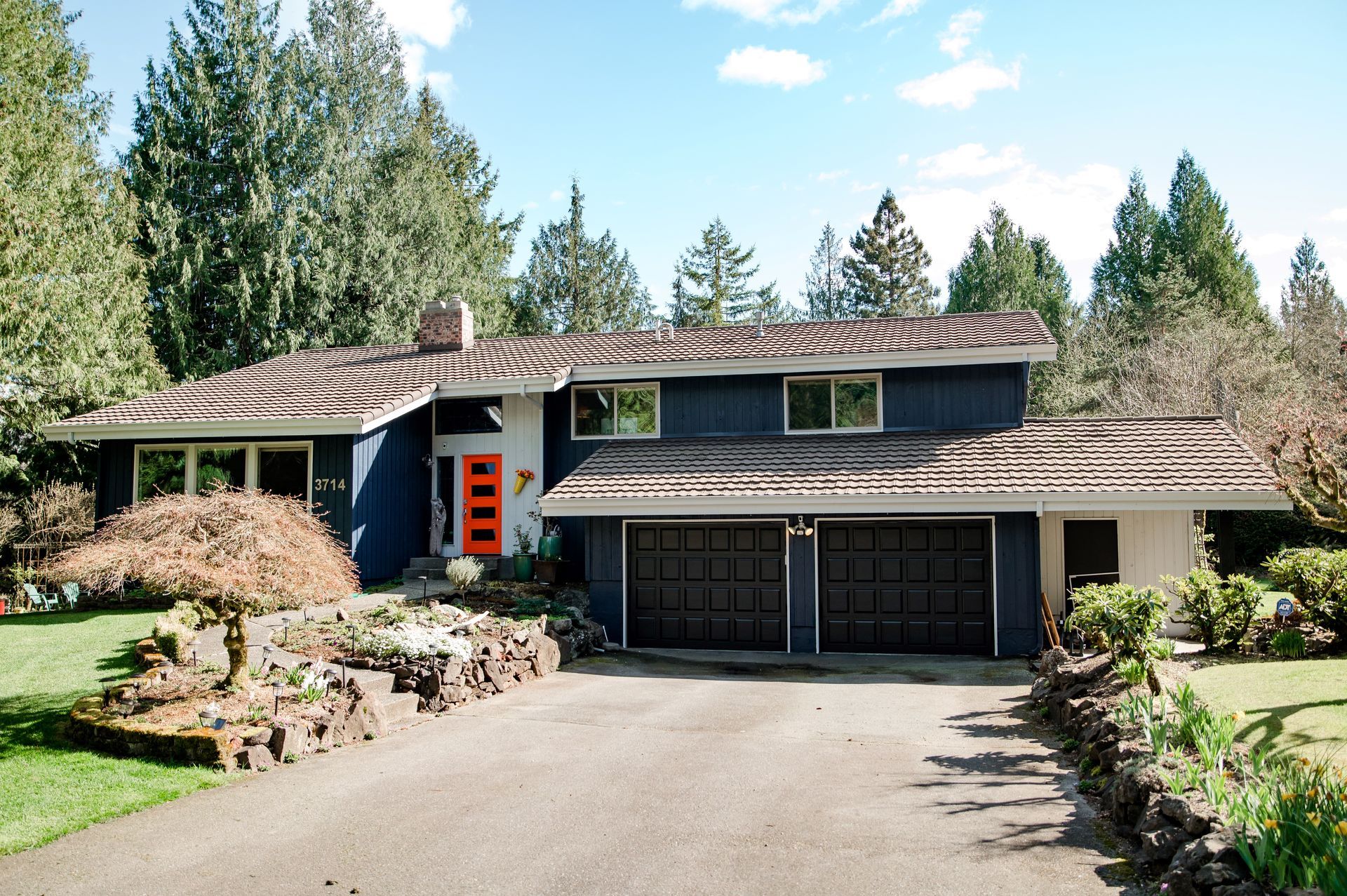 A blue house with an orange door is surrounded by trees