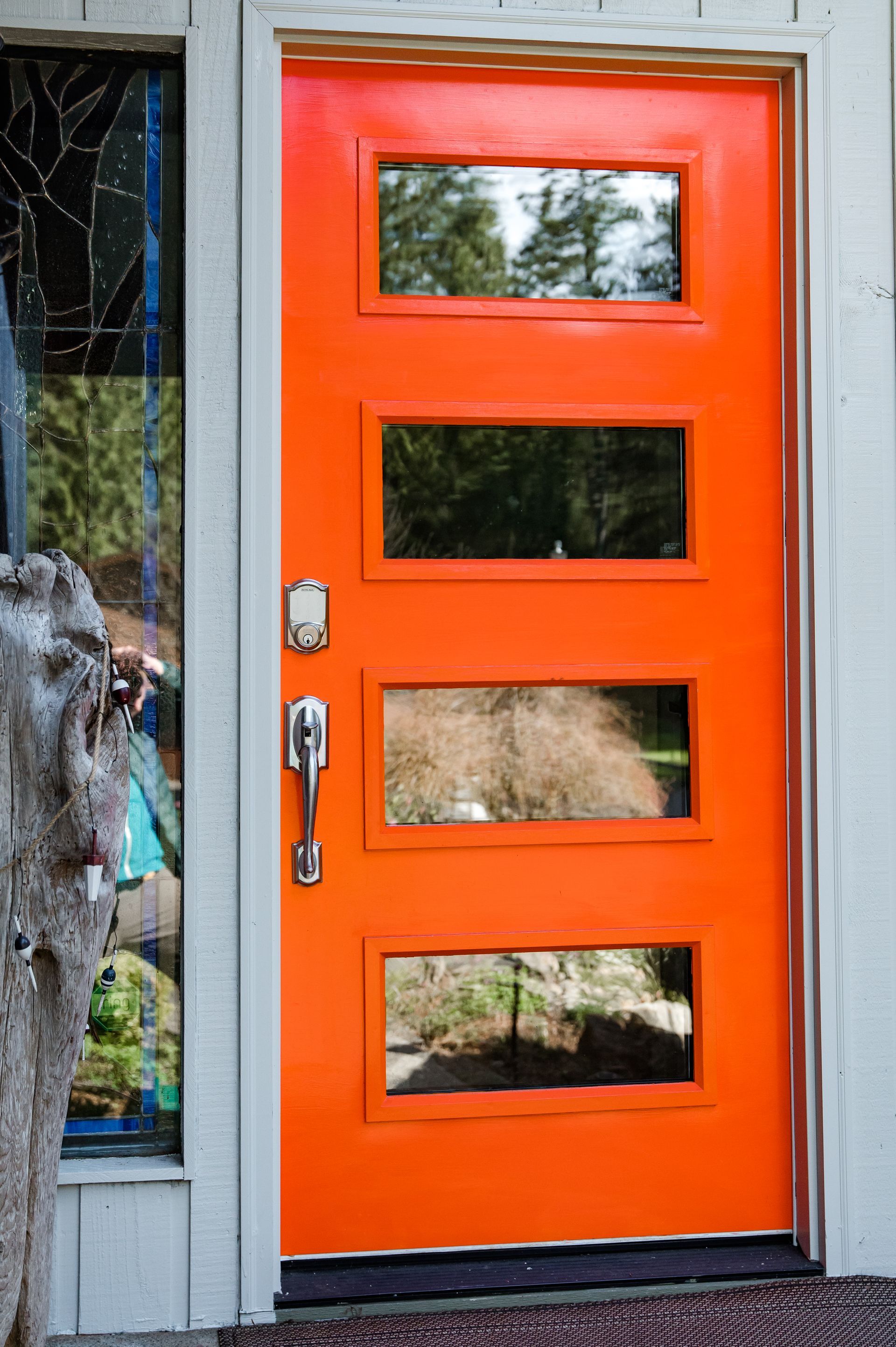 A bright orange door with four windows on a white house