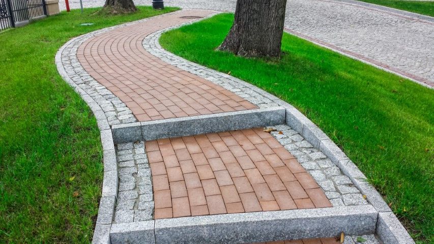 A pedestrian path features a single concrete step, transitioning from a curved section to a straight one.