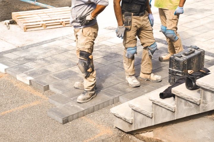 Three construction workers standing on a half-finished paved patio next to concrete steps.