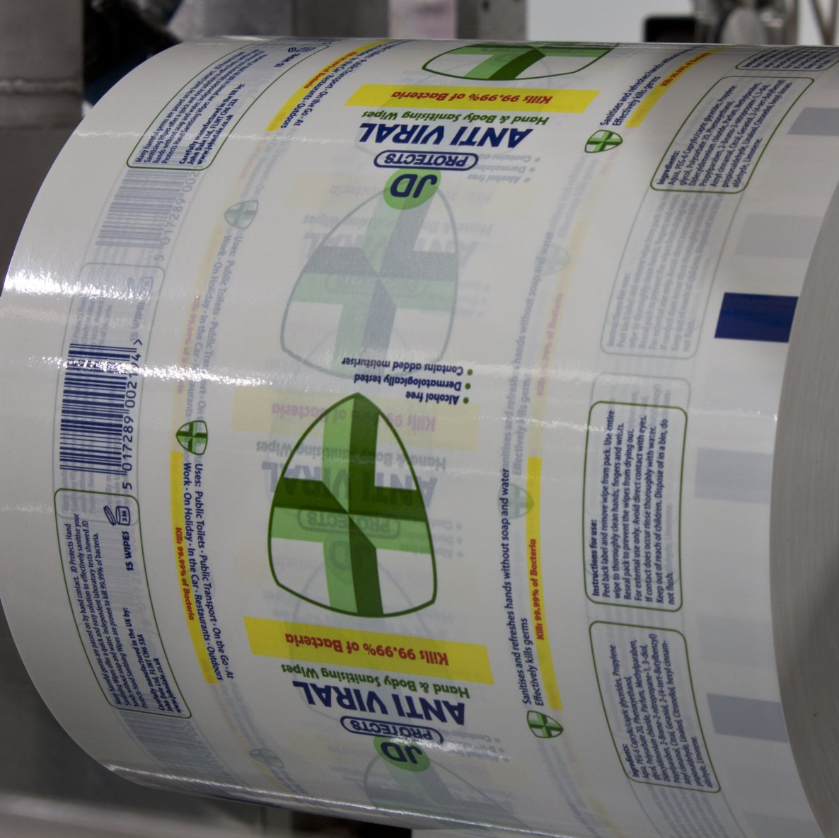 Roll of white anti-viral label material with green shield logos on a printing press spool.