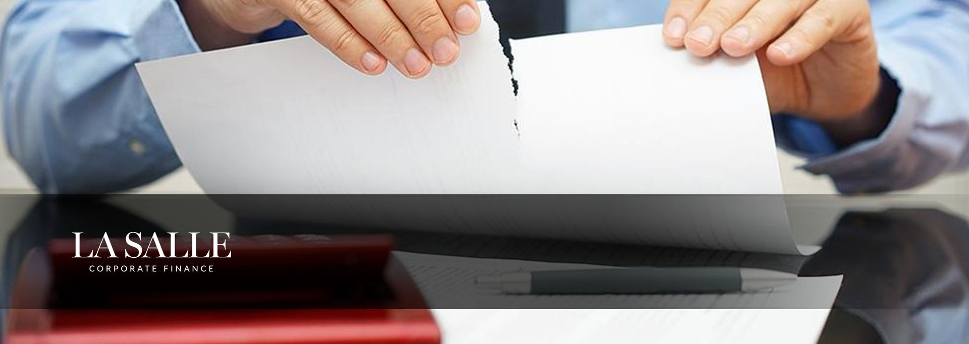 Hands tearing a white sheet of paper over a laptop with a dark business-themed banner below.