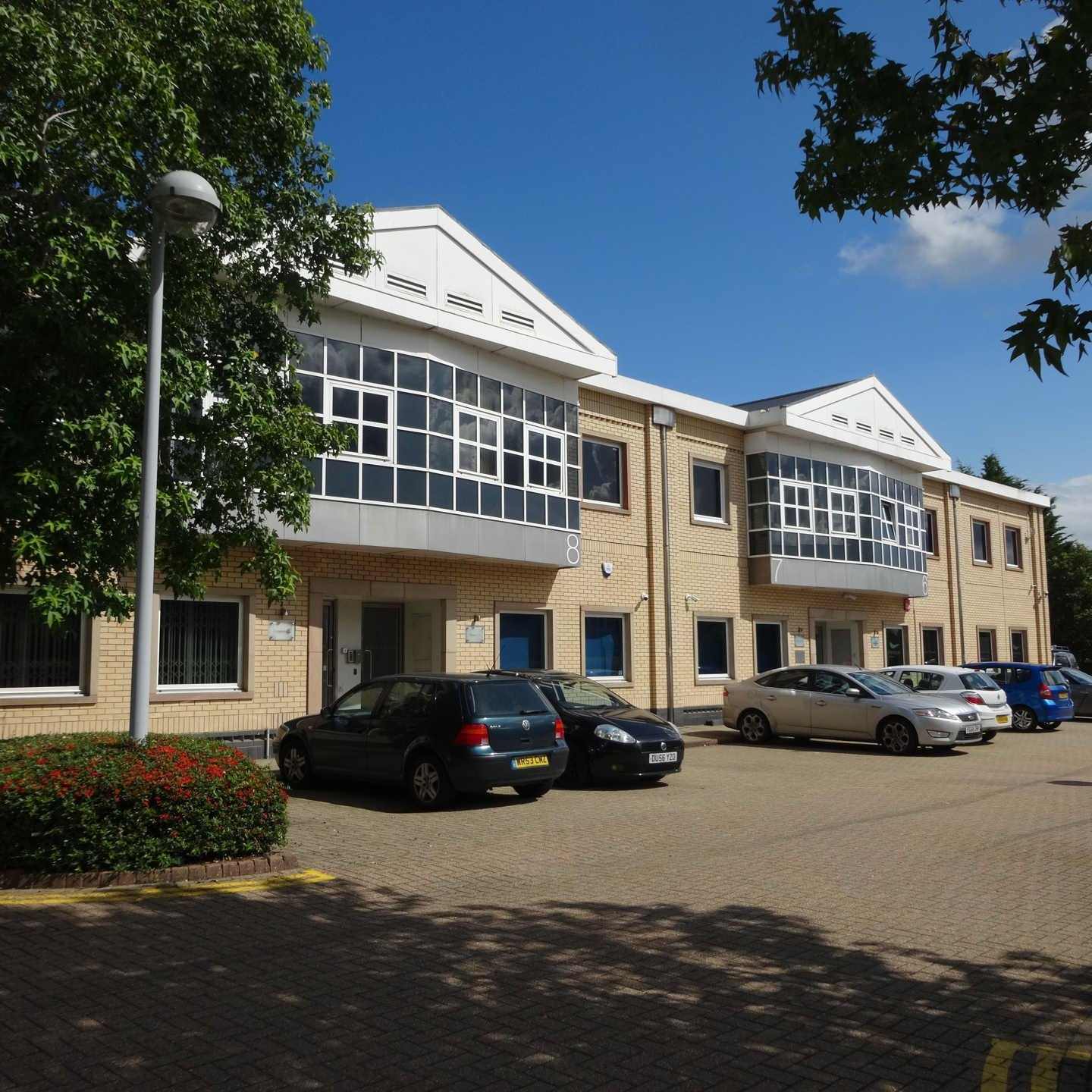 Two-story beige office building with parked cars under a sunny blue sky
