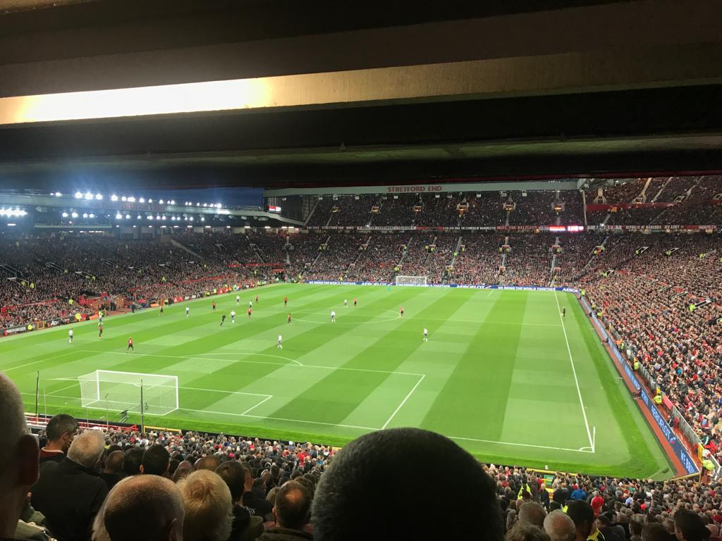 Packed soccer stadium at night, with a green pitch and players during a match.