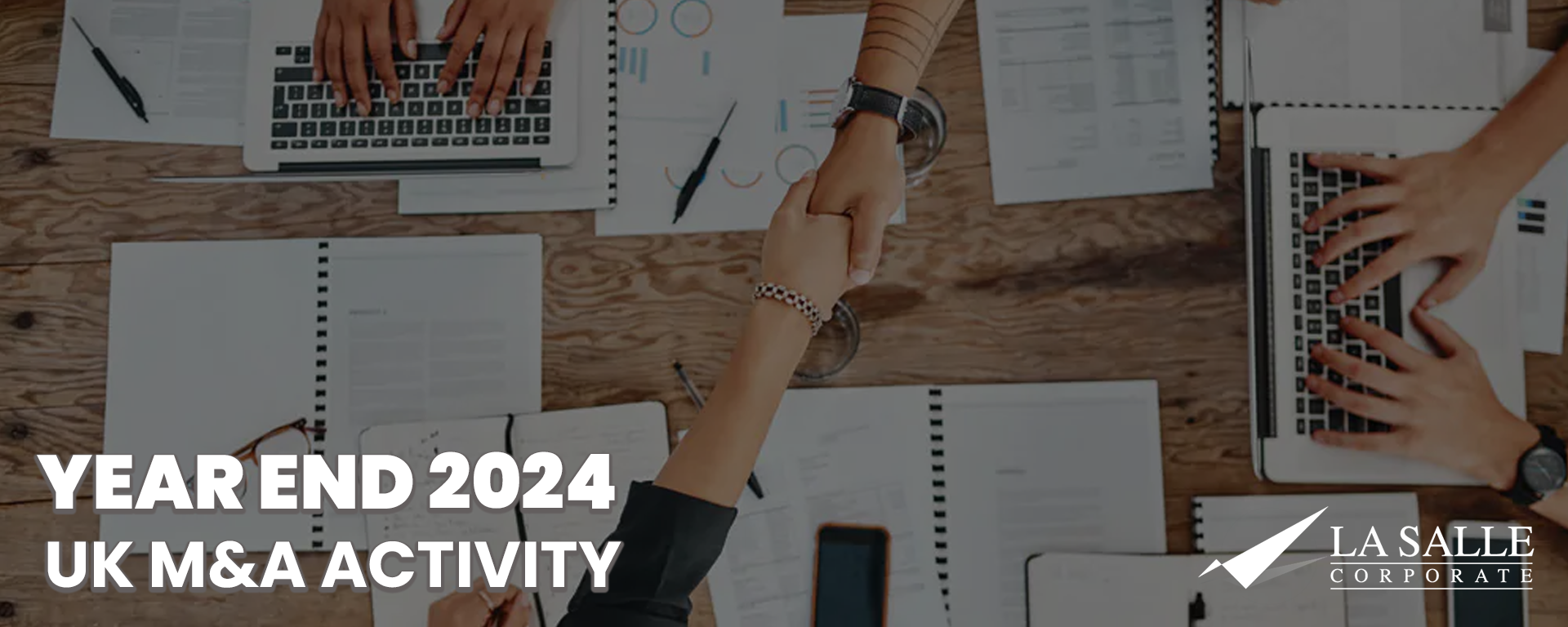 Hands around a table with documents and laptops, overlaid with “YEAR END 2024 UK M&A ACTIVITY” text.