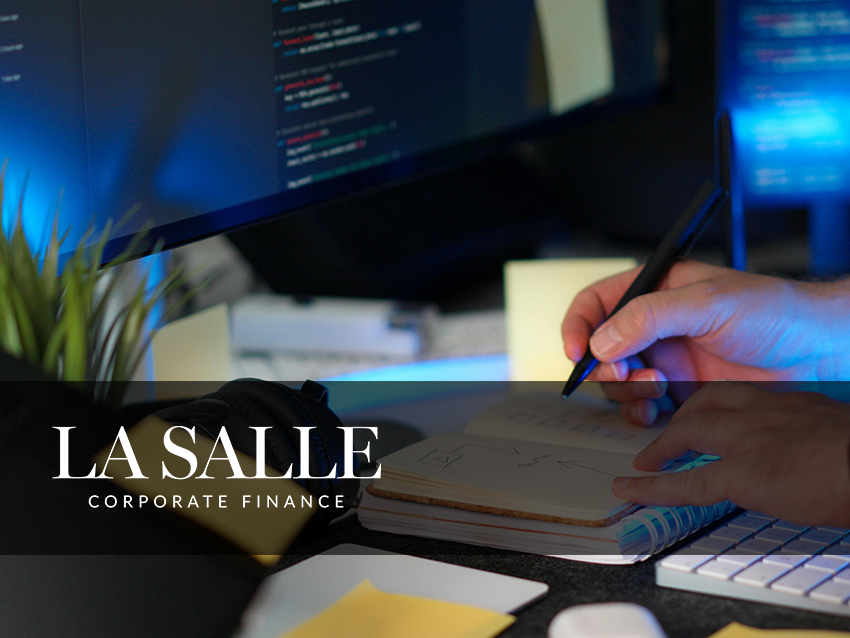 Corporate finance desk with hand writing in notebook, computer screens in background, and La Salle logo overlay
