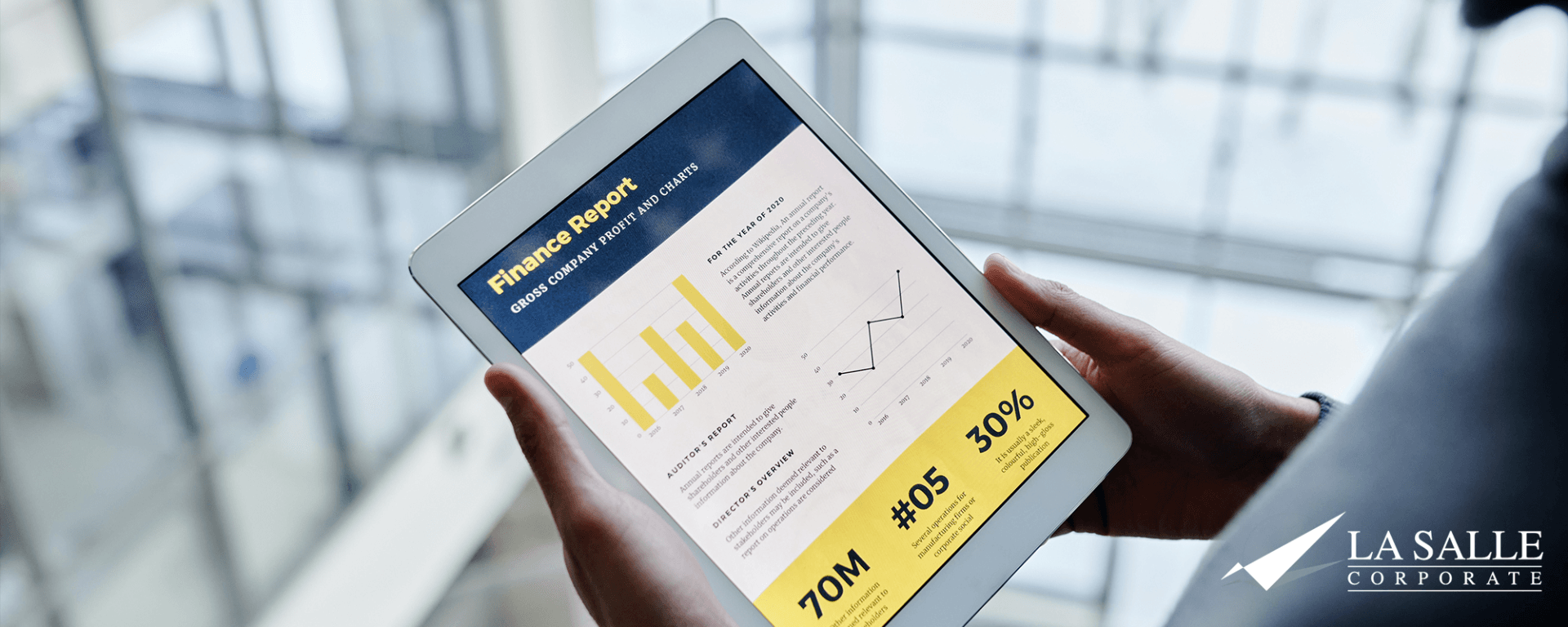 Hand holding a tablet showing charts and analytics in a bright office lobby