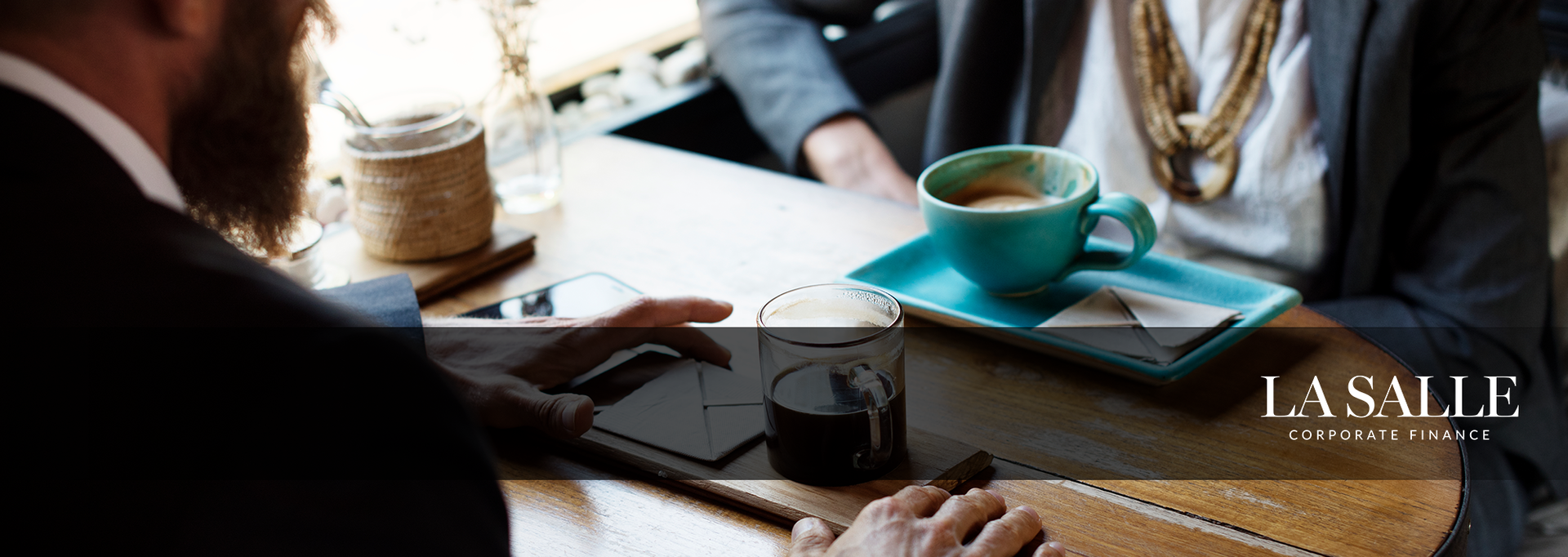 People meeting at a table with coffee and a notebook in a bright café setting