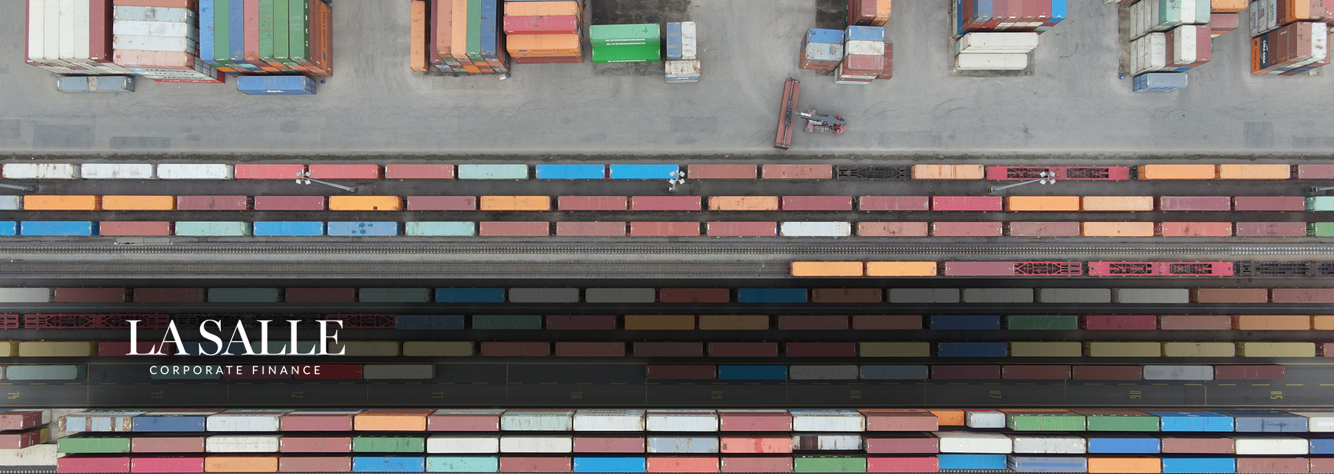Colorful shipping containers stacked in rows, forming an aerial view of a cargo yard with a striped roadway.