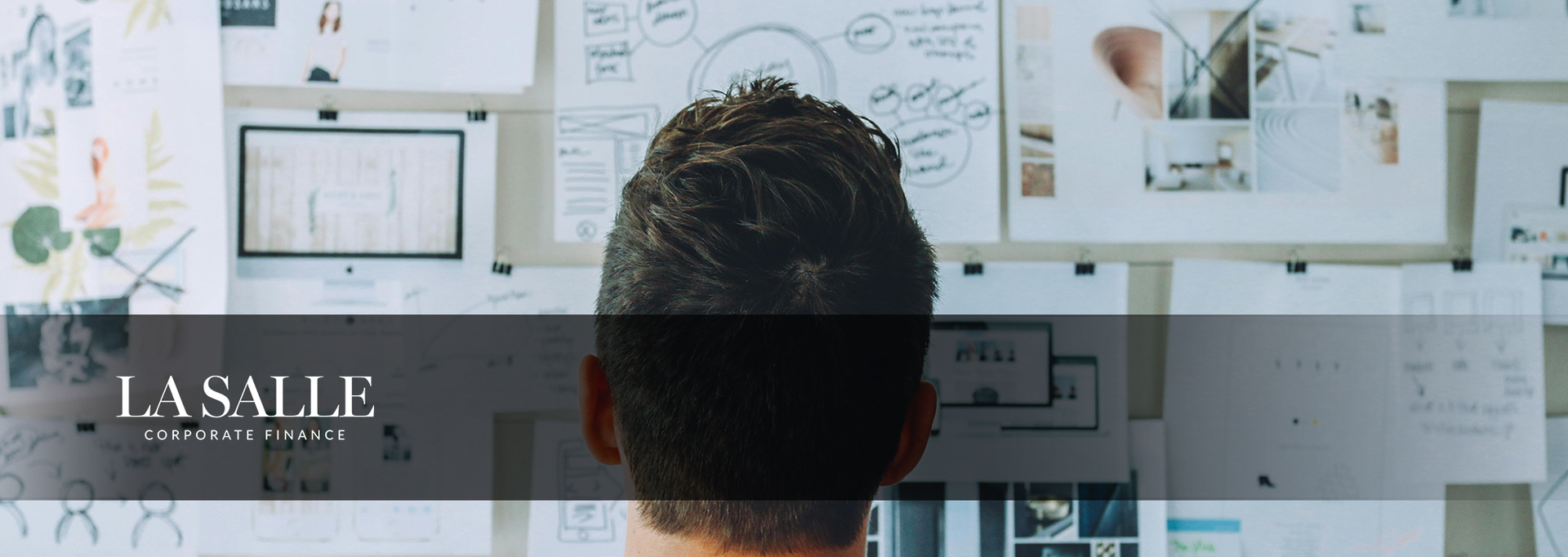 Person viewing a wall of design sketches and website mockups with a laptop in a bright office