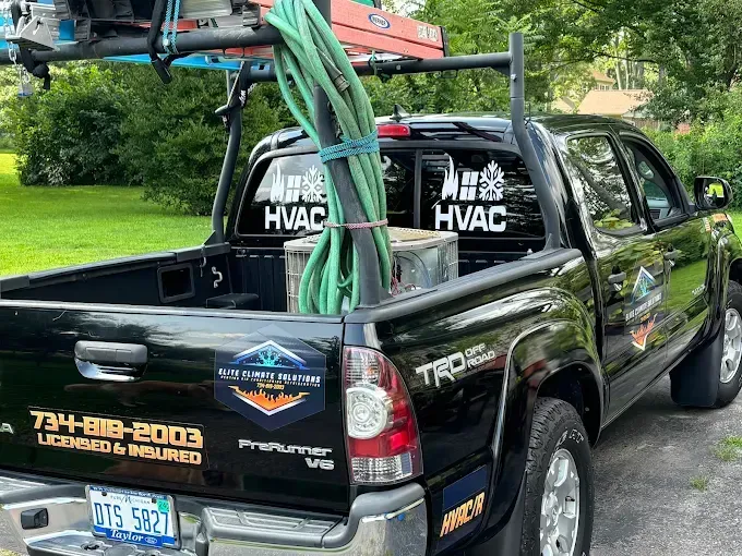 Black HVAC service truck with a ladder, hose, and company logos.