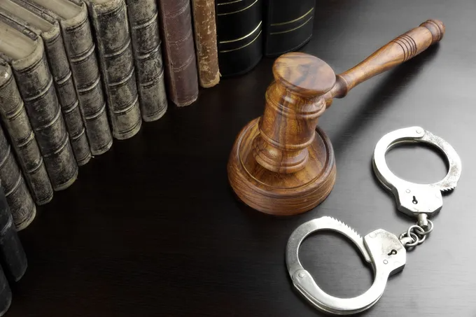 Gavel, handcuffs, and law books on a dark surface, symbolizing justice and legal proceedings.