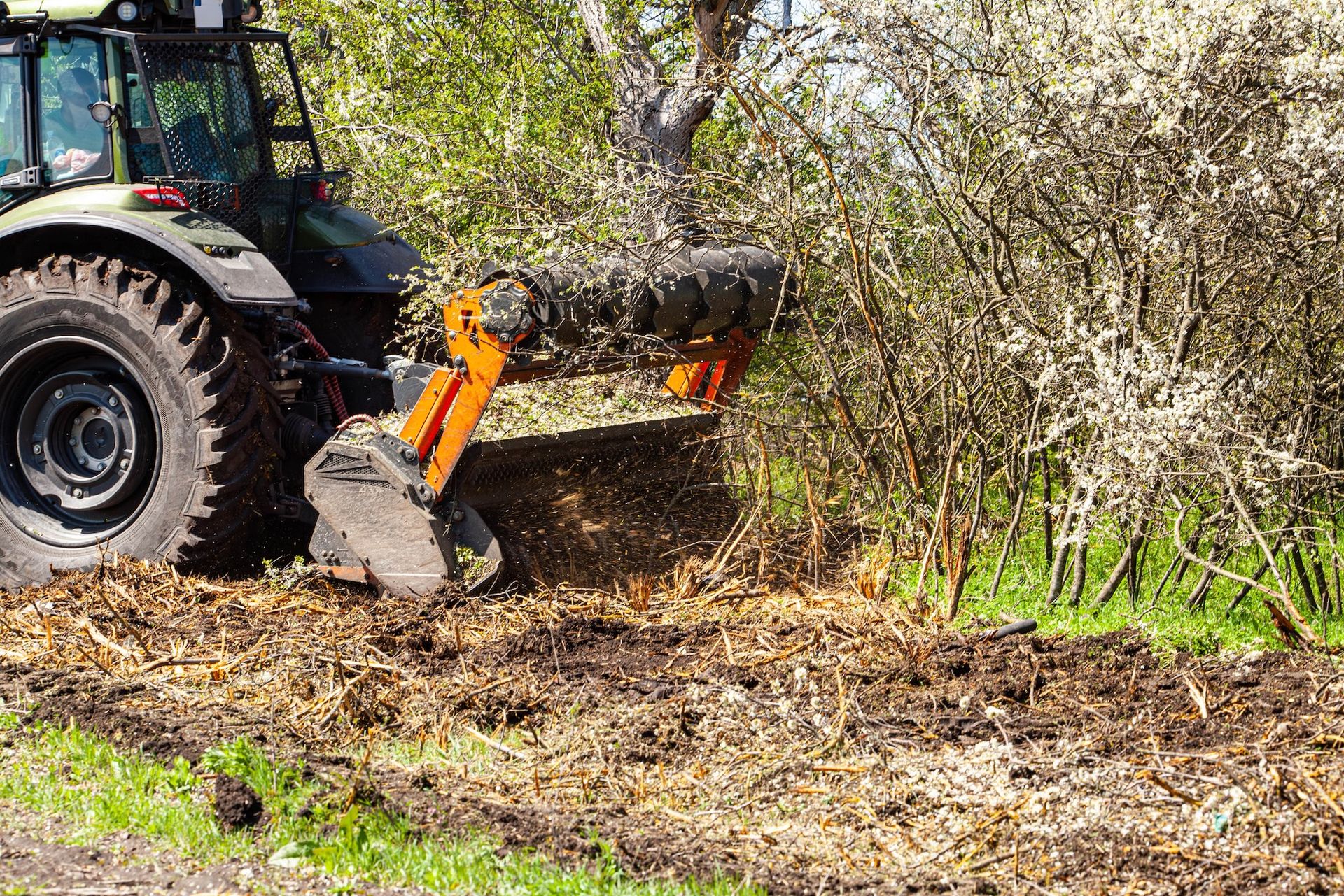 Tractor with a front-mounted brush cutter mulching vegetation near a field.