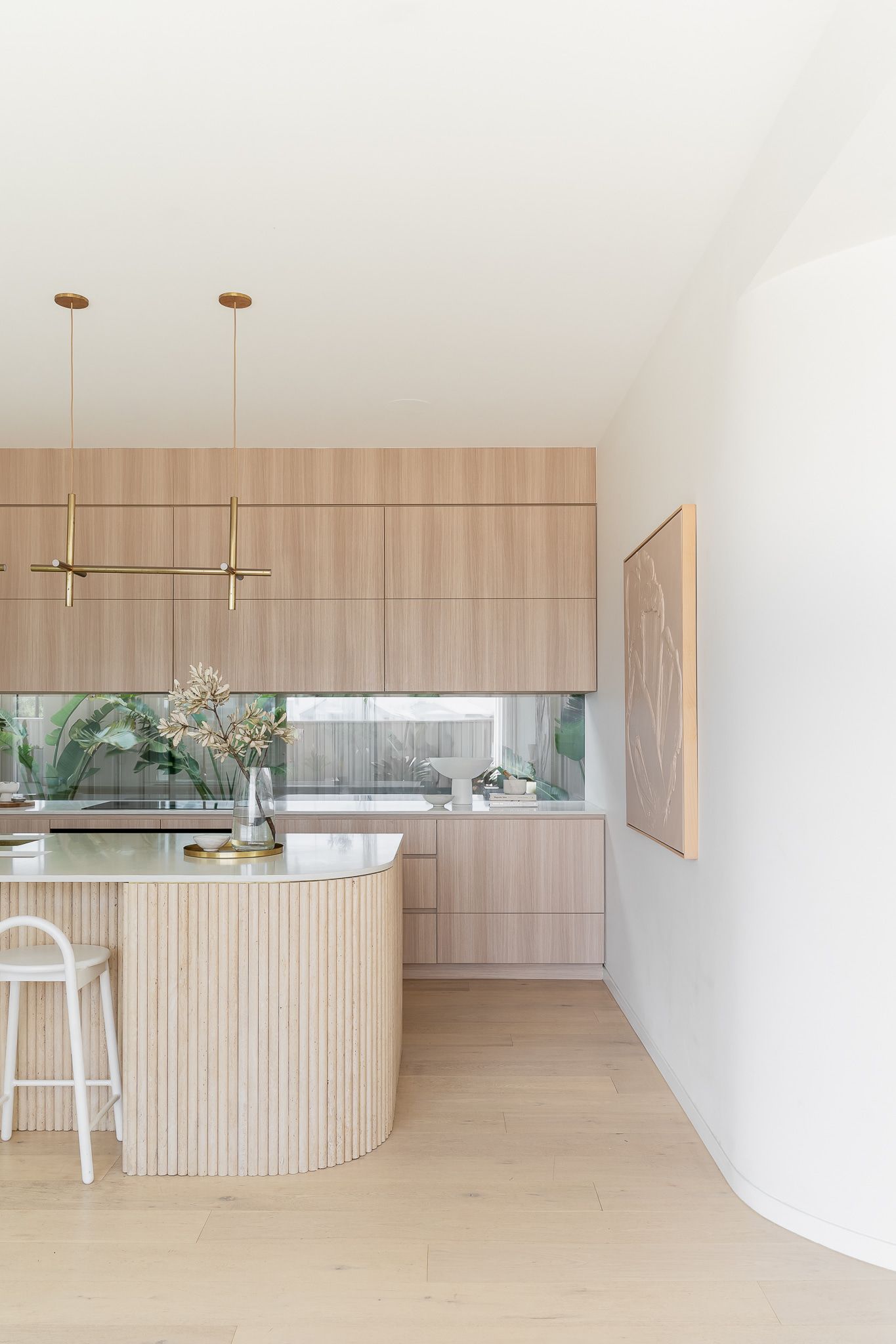 Light wood kitchen with curved island, white walls, and a window with greenery — SDC Building Design In Wollongong, NSW