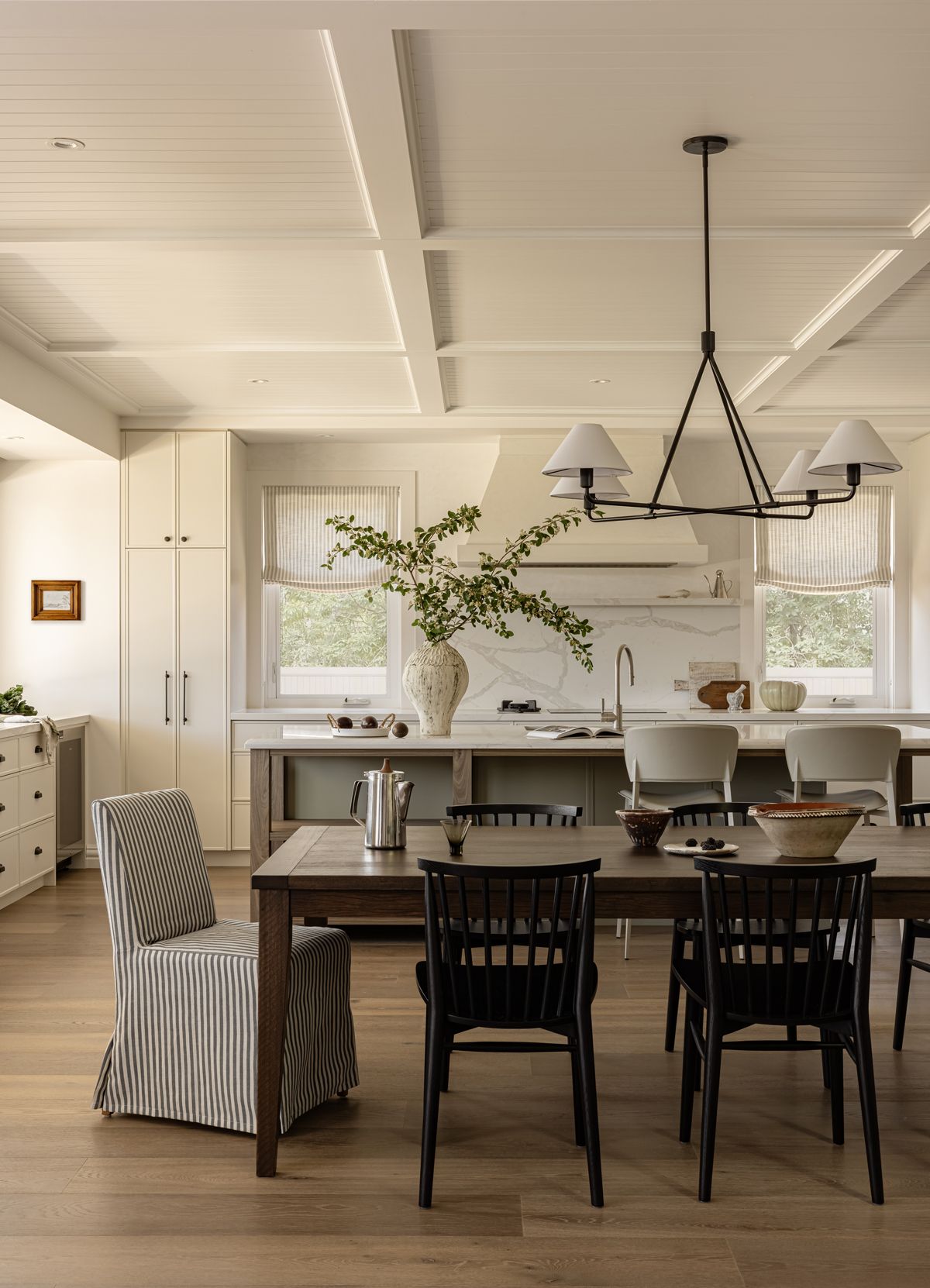 Dining room with wooden table, mixed chairs, and open kitchen with light neutral colours — SDC Building Design In Kiama, NSW