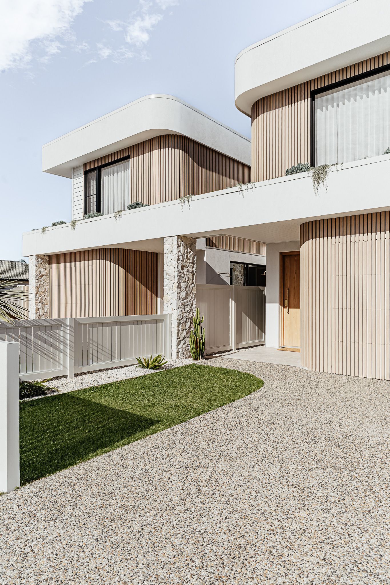 Modern house with curved white accents, vertical wooden siding, and a pebble pathway — SDC Building Design In Wollongong, NSW