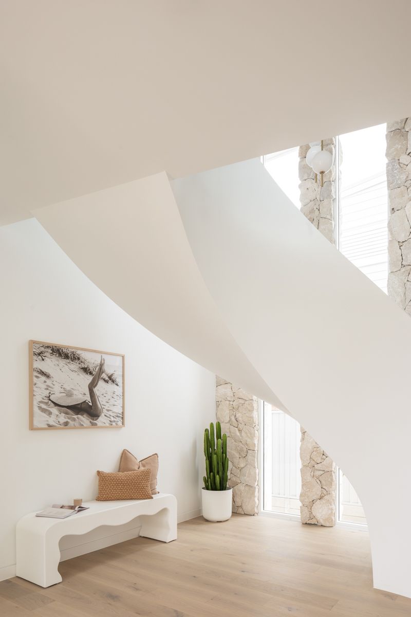 White, modern staircase with art, bench, cactus, and stone wall detail. Bright, airy interior — SDC Building Design In Wollongong, NSW