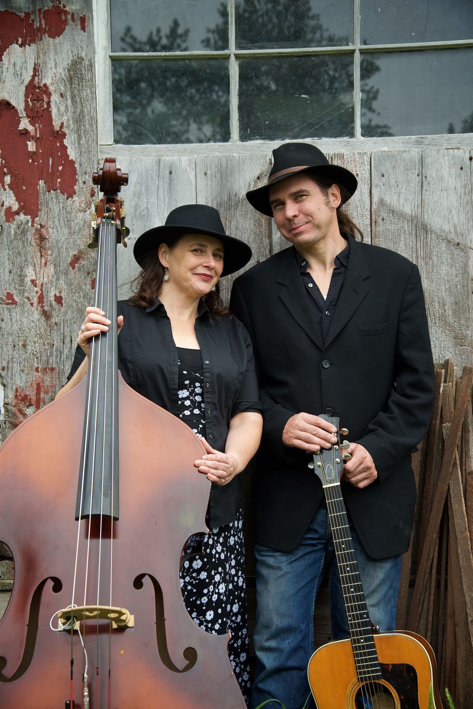 woman in hat with an instrument standing beside a man in hat  holding a guitar