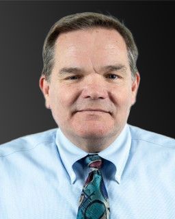 man with brown hair wearing a blue shirt and colored tie