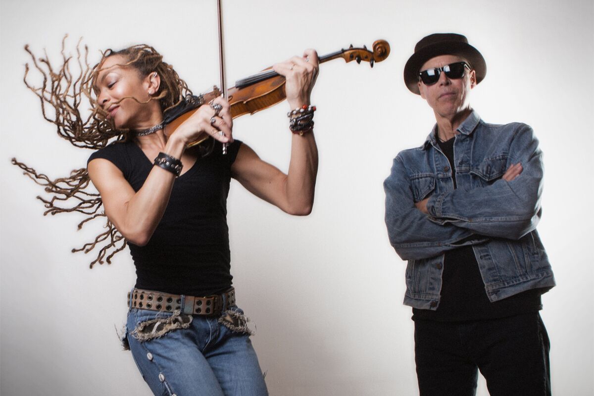 A woman playing a violin next to a man with his arms crossed