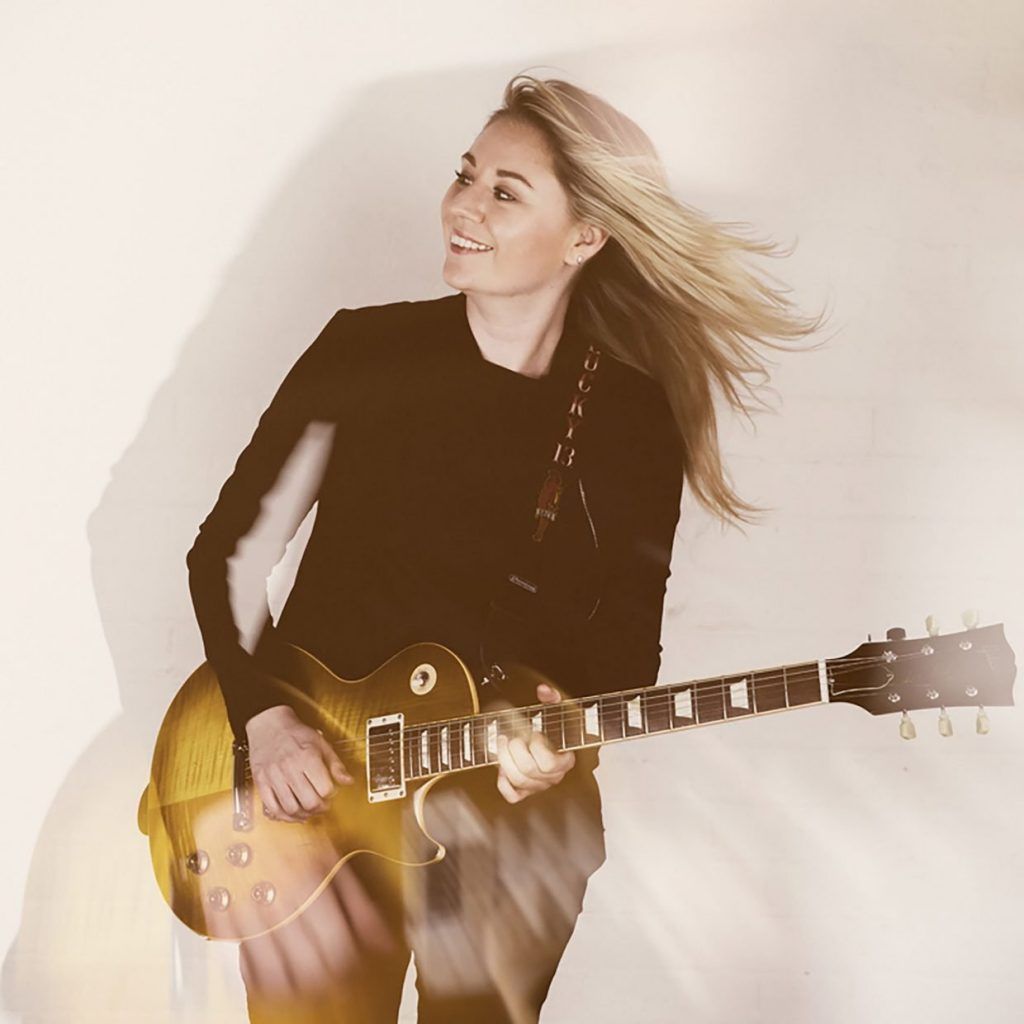 A woman in a black shirt is holding a guitar