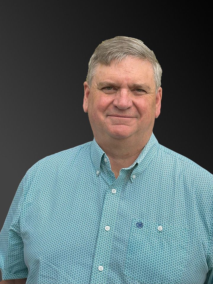 Man in blue patterned shirt smiling, with a dark background.