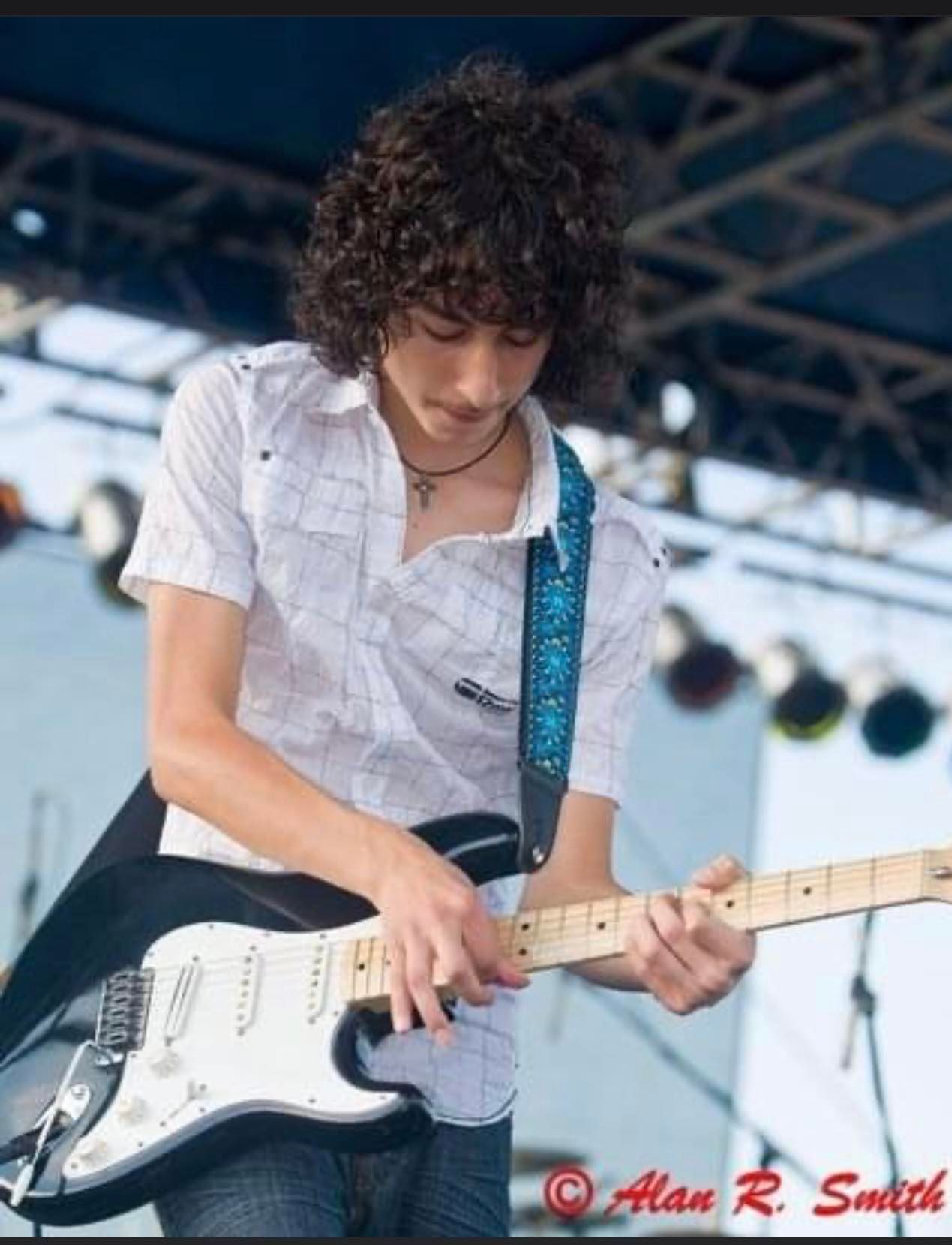 A young man with curly hair is playing a guitar in a photo by alan r. smith