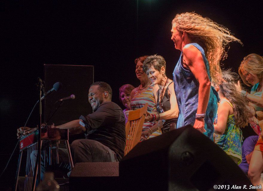 A group of people are standing around a man playing a keyboard on a stage.