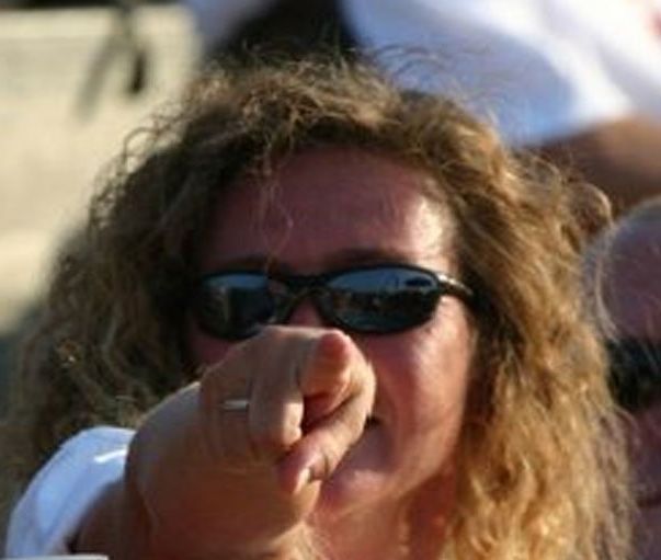 A woman wearing sunglasses is pointing at the camera.