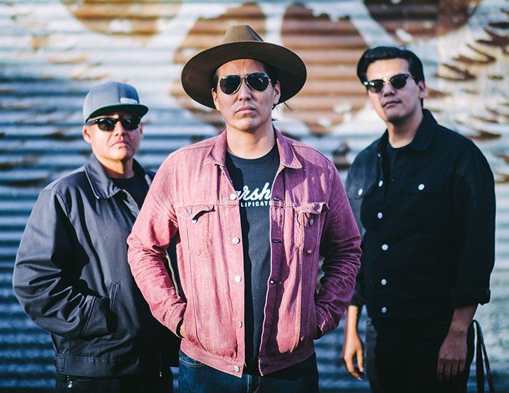 Levi Platero in a pink jean jacket posing with his band members,