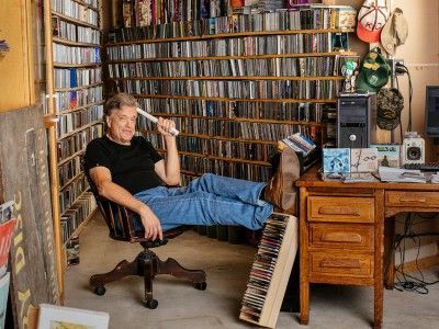 A man is sitting in a chair with his feet up in front of a bookshelf.
