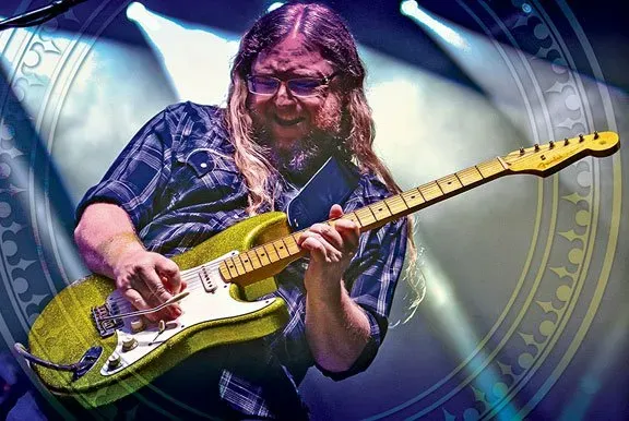 A man with long hair is playing a guitar on stage